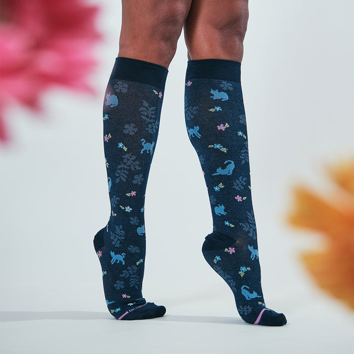 Knee-high compression socks featuring a dark background with colorful cat and floral patterns.
